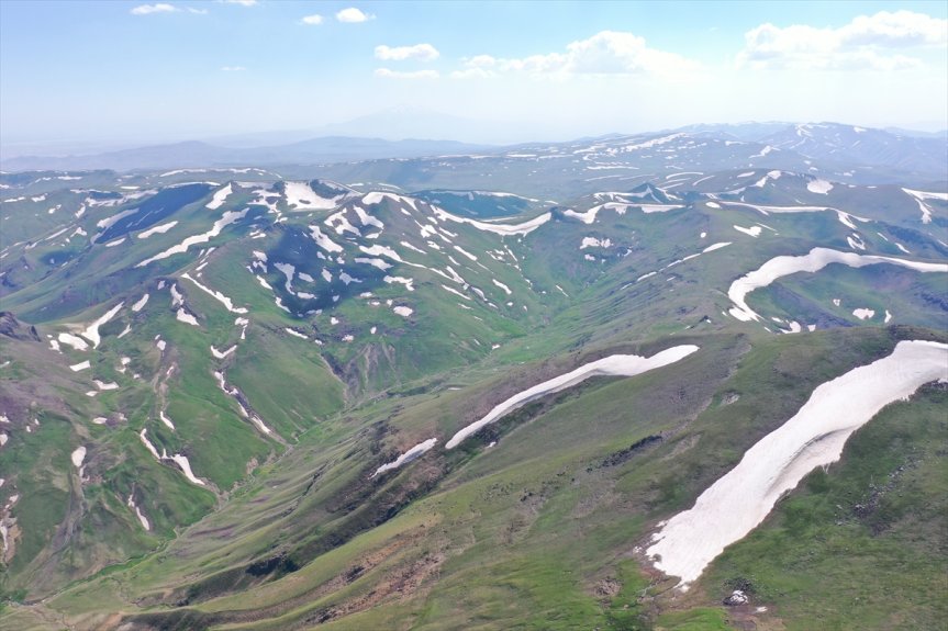 Ağrı'nın Taşlıçay ilçesinde kar izleriyle çevrili vadiler, yaz mevsiminde etkileyici bir dağ panoraması sunuyor.