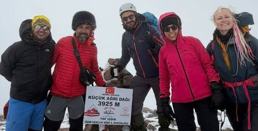 Beş dağcı, Küçük Ağrı Dağı'nın 3925 metre yüksekliğindeki karlı zirvesinde tabela önünde hatıra fotoğrafı çektiriyor.